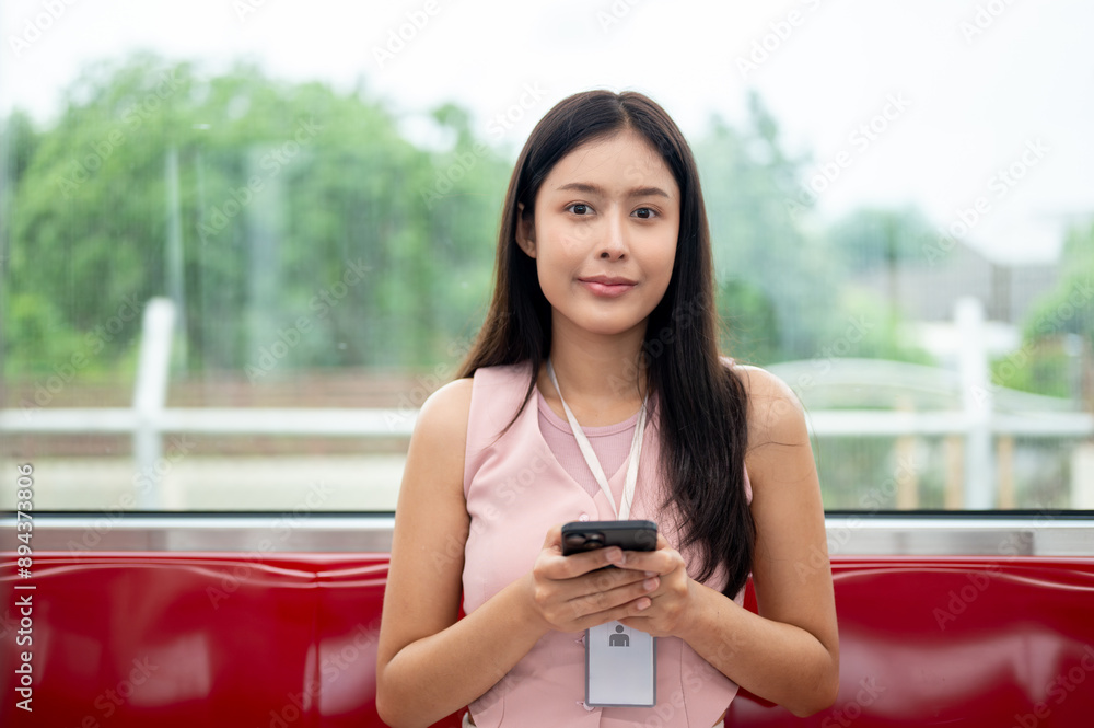 A positive Asian female office employee with a phone in her hand is sitting in a seat on a sky train A positive Asian female office employee with a phone in her hand is sitting in a seat on a sky train