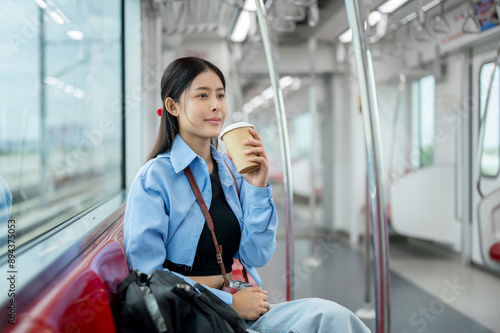 Tableau sur toile A happy Asian female passenger is sipping coffee while commuting in the city with a sky train