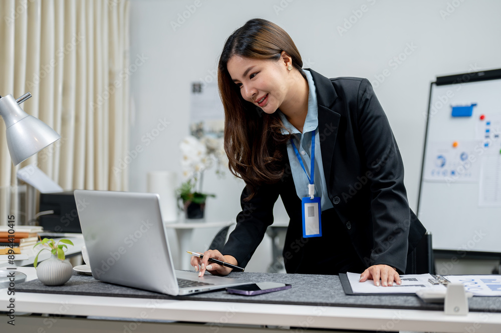 An attractive Asian businesswoman is standing and working on her laptop at her desk. An attractive Asian businesswoman is standing and working on her laptop at her desk.