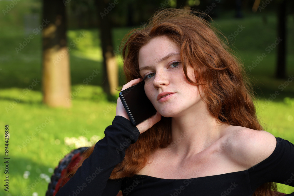 Attractive girl with long ginger hair talking on mobile phone in summer park Attractive girl with long ginger hair talking on mobile phone in summer park