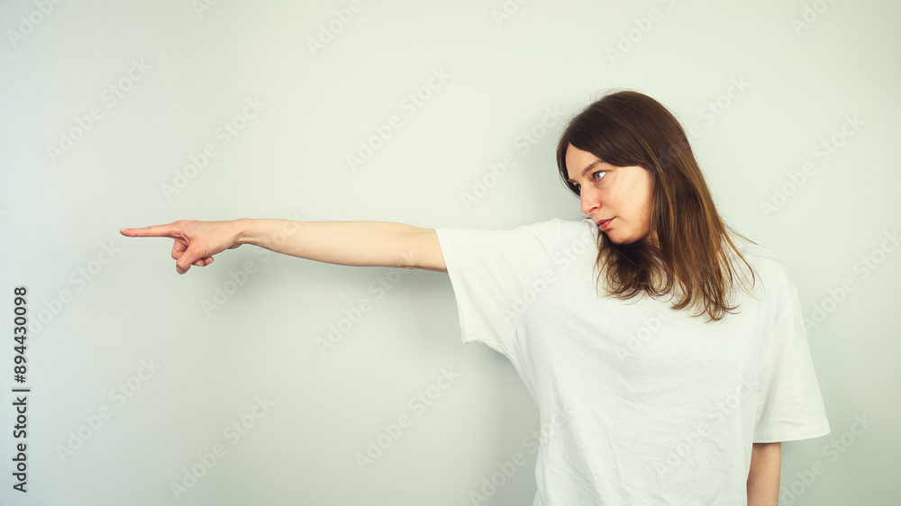 Portrait of beautiful Caucasian young female model with blue eyes and white shirt pointing her finger, direction gesture, isolated on white background, copy space area
