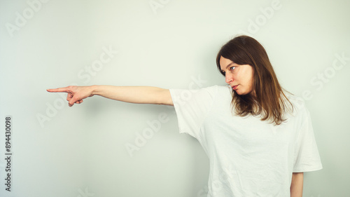 Obraz na płótnie Portrait of beautiful Caucasian young female model with blue eyes and white shirt pointing her finger, direction gesture, isolated on white background, copy space area w salonie