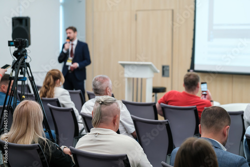 Business presentation held in conference room with speaker addressing audience, recorded by camera.