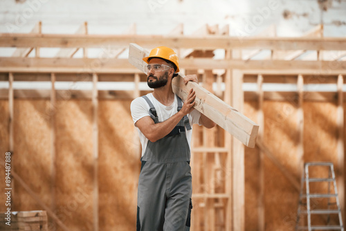 Walking, holding plank. Industrial worker in wooden warehouse