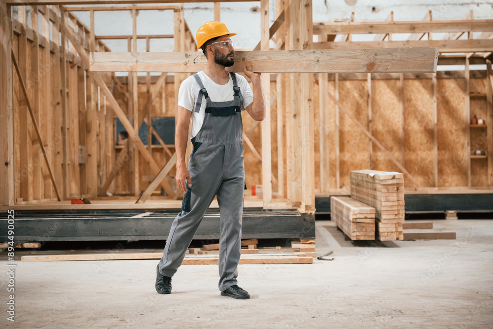 Fototapeta premium Going and carrying plank. Industrial worker in wooden warehouse