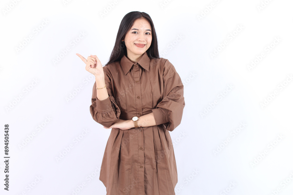 Beautiful young Asian woman wearing brown shirt pointing finger aside copy space isolated on white background. Beautiful young Asian woman wearing brown shirt pointing finger aside copy space isolated on white background.