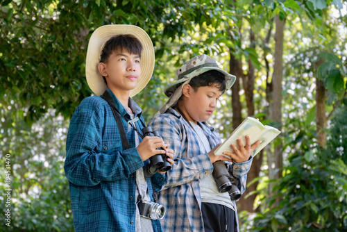 Asian children using binoculars to do the birdwatching in tropical forest during summer camp, idea for learning creatures, wildlife animals and insects outside the classroom.