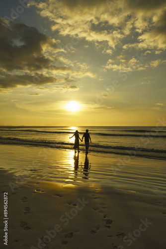 Kota Kinabalu, Sabah, Malaysia - February 4, 2016: Sunset view of a couple tourist standing on sandy beach with footprints against sea horizon
 photo