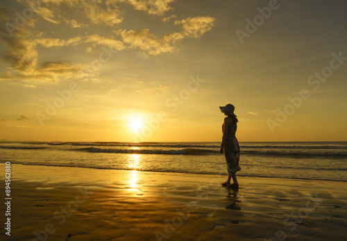 Kota Kinabalu, Sabah, Malaysia - February 2, 2016: Summer and sunset view of a female tourist in skirt standing on sandy beach against sea horizon
 photo