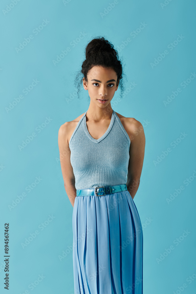A young Black woman in a dress stands against a bright blue background. A young Black woman in a dress stands against a bright blue background.