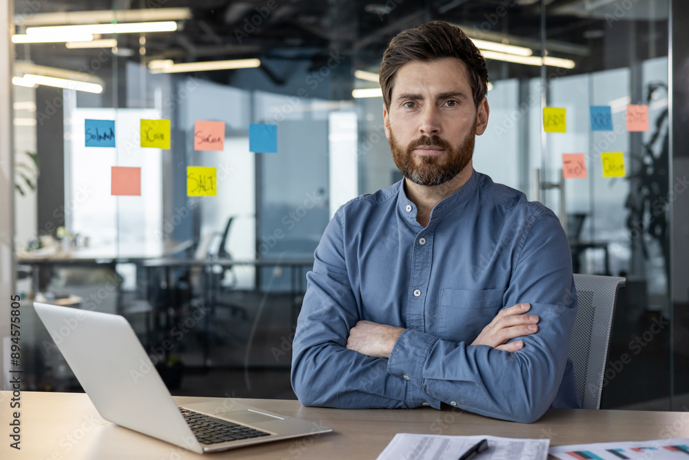 Business professional in blue shirt sitting at office desk with laptop and charts Business professional in blue shirt sitting at office desk with laptop and charts