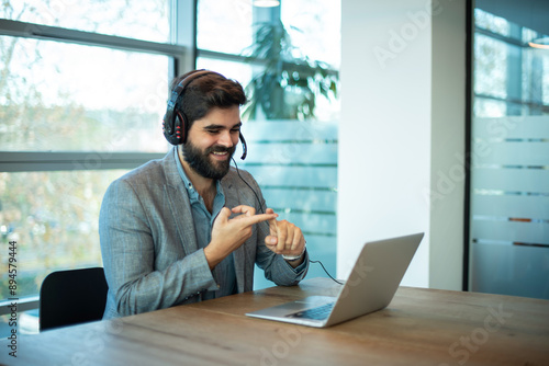 Wallpaper Mural Smiling male consultant of call center with headset having a video call meeting via laptop in office. Torontodigital.ca