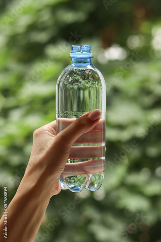 A bottle with a stationary plastic cap in a woman's hand and trees with a blurred background .  High quality photo
