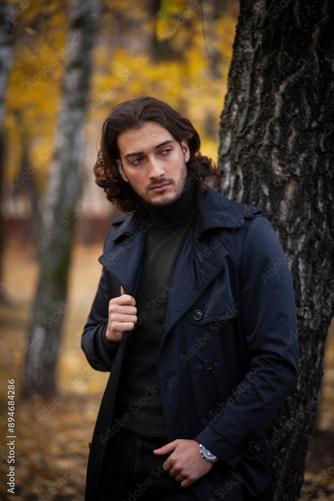 Portrait of handsome long haired man in black trench coat in the park in wonderful autumn day. Fashion and style concept Portrait of handsome long haired man in black trench coat in the park in wonderful autumn day. Fashion and style concept
