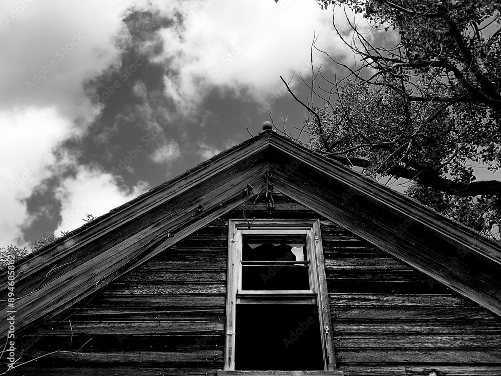 Obraz premium Black and white photo of a roof and broken window belonging to an abandoned farmhouse in rural North Dakota