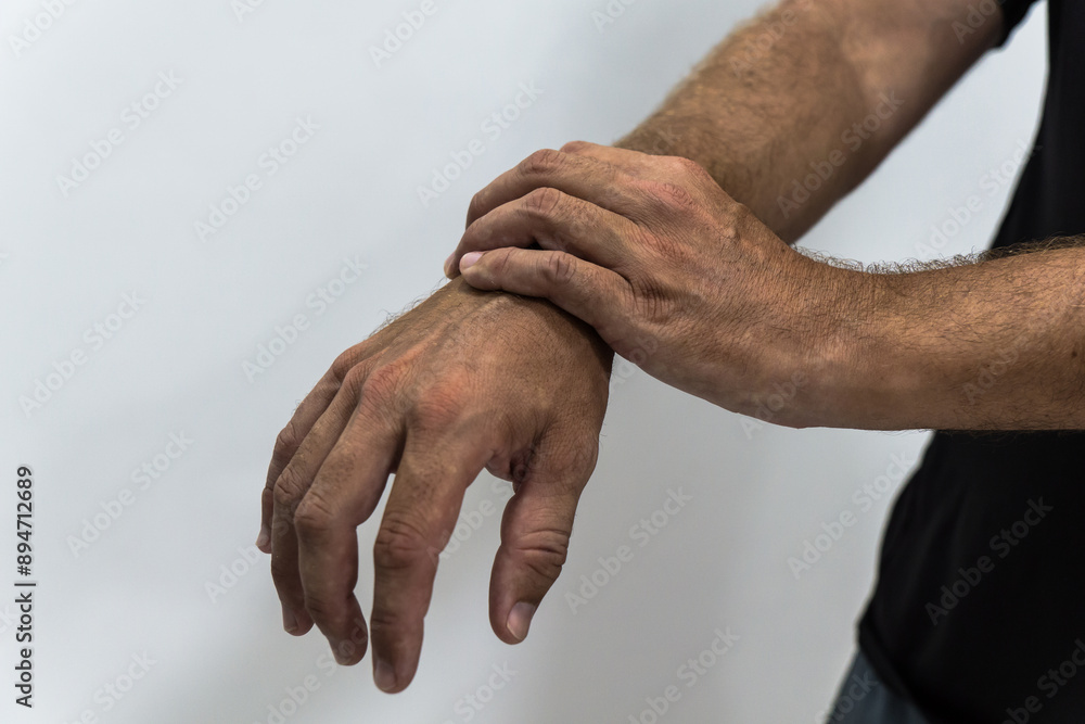 Fototapeta premium Close up of a man suffering from inflammation, massaging his wrist over white background. By repetitive movements. Work-related pathologies