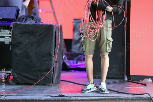 Worker gathering cables on stage. Electrician working on a stage. Man working at event. Technician preparing the lighting wiring for a musical show on stage.