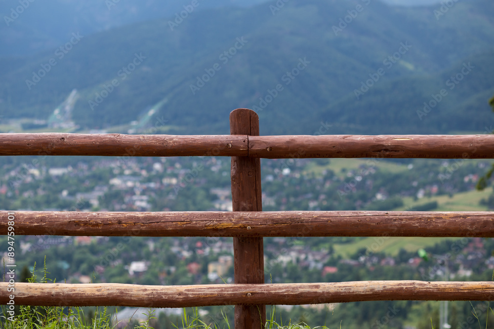 Obraz premium Green mountain slopes. Forest on the mountainside. A high wooden fence in front of a cliff.
