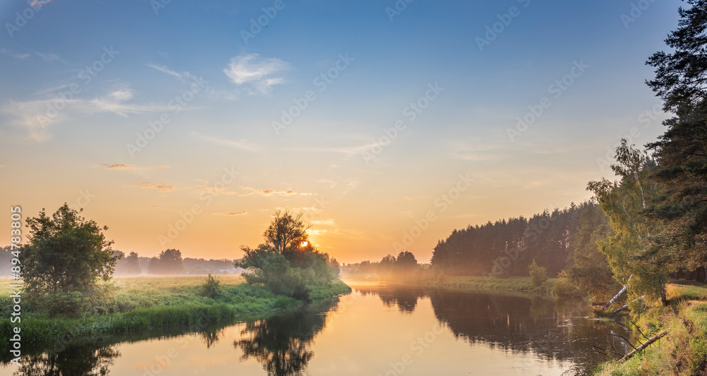 Fototapeta premium A beautiful sunset over a river with trees in the background