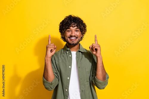 Portrait photo of young latin student guy in khaki shirt point fingers above promotion isolated on yellow color background photo
