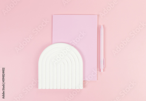 Top view of pink notebook, pink pen, white arch tray on pink background. School, office wallpaper. Flat lay, copy space.