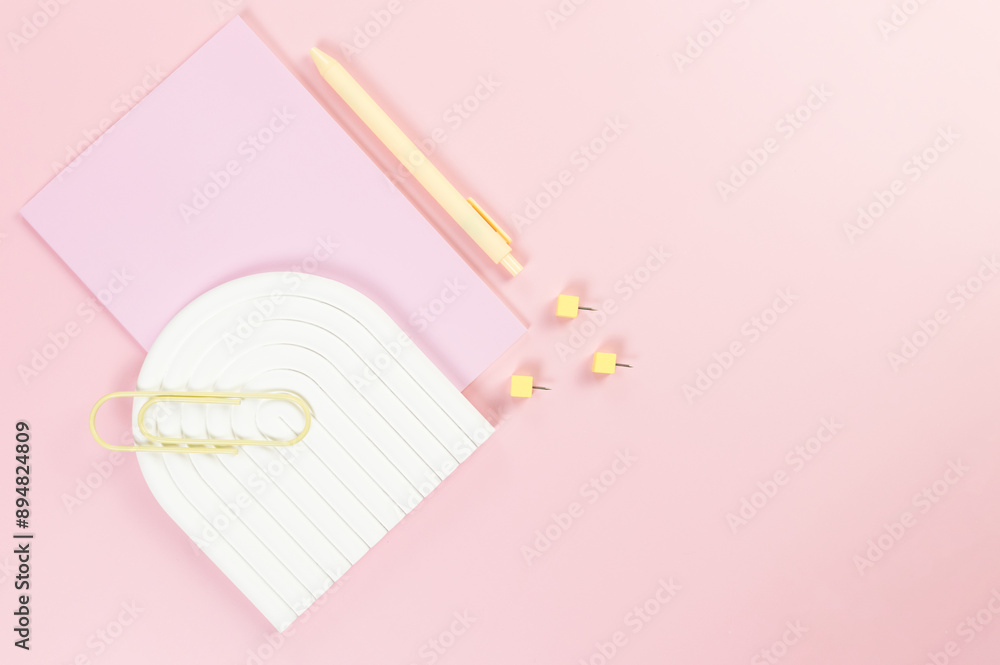 Top view of pink notebook, yellow pen, paperclip, pins, white arch tray on pink background. School, office wallpaper. Flat lay, copy space. Top view of pink notebook, yellow pen, paperclip, pins, white arch tray on pink background. School, office wallpaper. Flat lay, copy space.