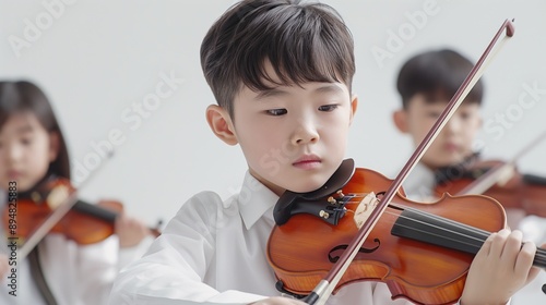 Asian boy concentrating on playing violin with classmates