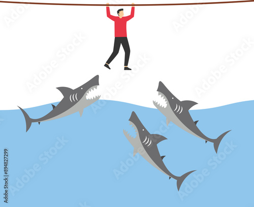 Businessman hangs on for dear life from a rope as he swings above a group of circling sharks in the sea. Risk taker, challenge to success, overcome difficulty or problem in crisis or entrepreneurship. photo