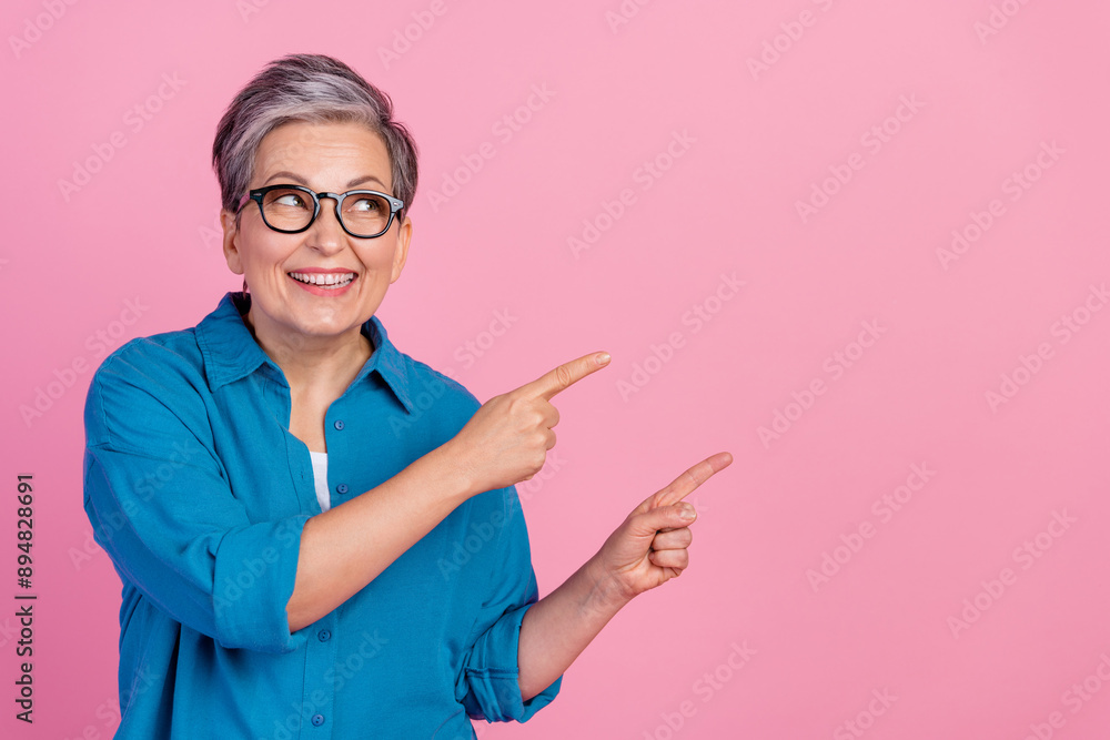 Photo portrait of attractive senior woman look point interested empty space dressed stylish blue clothes isolated on pink color background Photo portrait of attractive senior woman look point interested empty space dressed stylish blue clothes isolated on pink color background