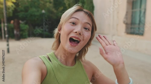 Friendly young woman say hi and wave hand cheerfuly smiling at camera photo