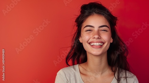 a stylish brunette woman in a casual pose, smiling and talking to a friend, against a vibrant red background