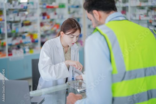 A female pharmacist is talking with a construction worker who needs medicine for pain and discomfort. Pharmacist in a pharmacy with medicines on shelves