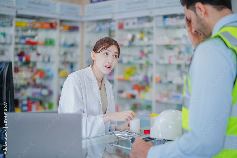 A female pharmacist is talking with a construction worker who needs medicine for pain and discomfort. Pharmacist in a pharmacy with medicines on shelves A female pharmacist is talking with a construction worker who needs medicine for pain and discomfort. Pharmacist in a pharmacy with medicines on shelves
