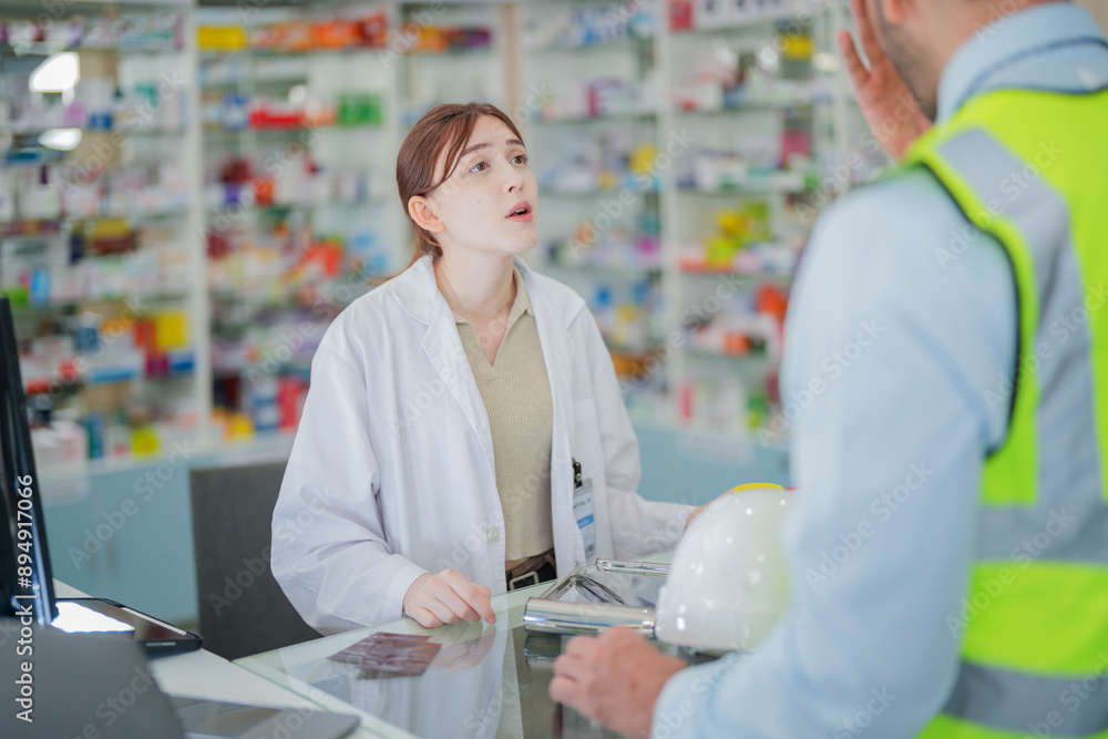 Obraz premium A female pharmacist is talking with a construction worker who needs medicine for pain and discomfort. Pharmacist in a pharmacy with medicines on shelves