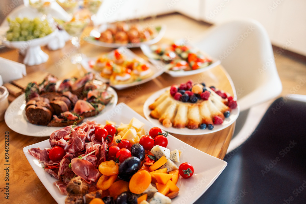 Close-up of delicious snacks on a wooden table in the dining room at home. Tasty hearty dishes. Sausage and cheese slicing with olives and tomatoes. Close-up of delicious snacks on a wooden table in the dining room at home. Tasty hearty dishes. Sausage and cheese slicing with olives and tomatoes.