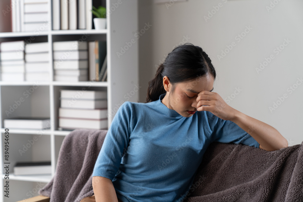 A photograph depicting a female individual in a state of discomfort seated upon a sofa within a residential setting. A photograph depicting a female individual in a state of discomfort seated upon a sofa within a residential setting.