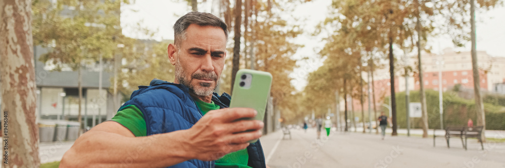 Fototapeta premium Mature man tourist wearing casual clothes sitting on bench scrolling smartphone