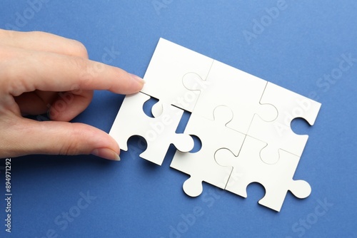 Woman solving white puzzle on blue background, top view