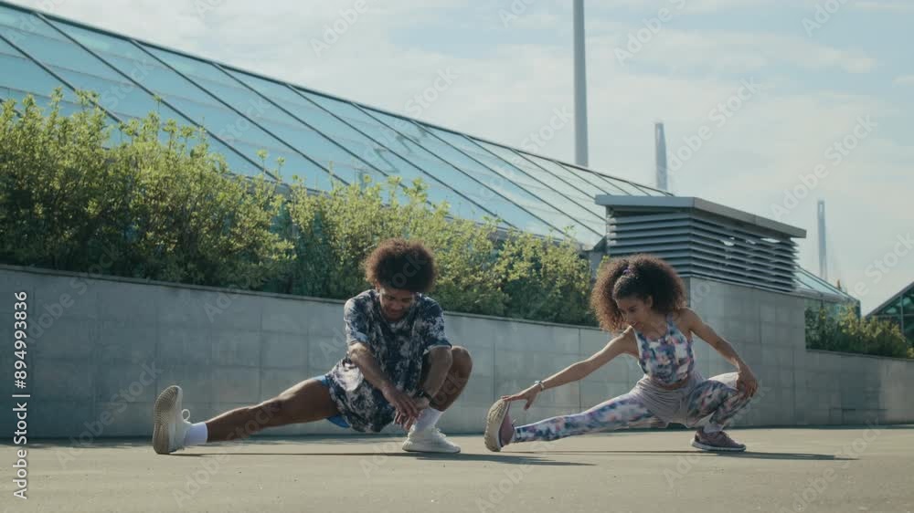 Young athletic couple in sportswear doing side lunge stretch and reaching their toes while warming up before outdoor workout on urban street Young athletic couple in sportswear doing side lunge stretch and reaching their toes while warming up before outdoor workout on urban street
