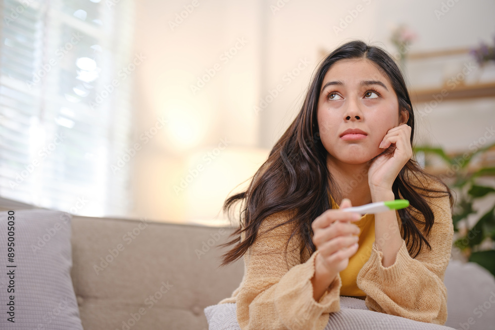 A woman is sitting on a couch with a pregnancy test in her hand A woman is sitting on a couch with a pregnancy test in her hand