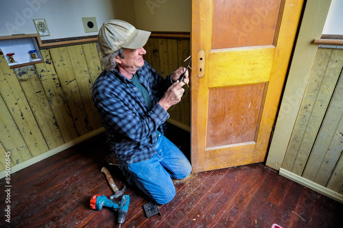 Carpenter installs a renovated door in a farmhouse; Dunbar, Nebraska, United States of America photo