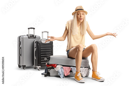 Confused young woman sitting on top of an overpacked suitcase photo