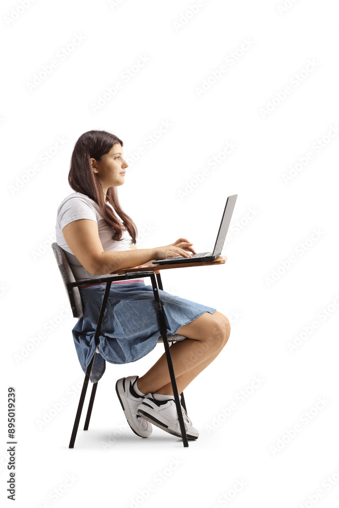 Teenage girl sitting in a school chair and using a laptop computer Teenage girl sitting in a school chair and using a laptop computer