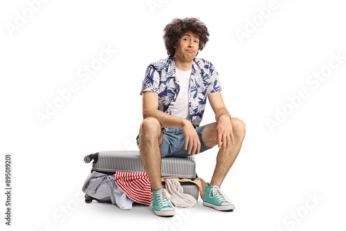 Young man sitting on a suitcase full of clothes photo