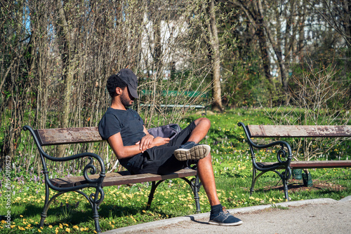 Capture the essence of urban tranquility with this photo of an individual enjoying a peaceful moment on a park bench surrounded by vibrant greenery and the soft hues of spring flowers.