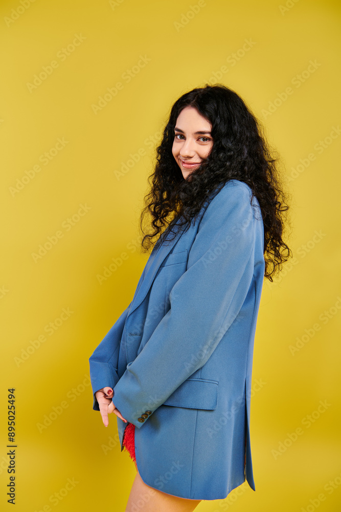 A young brunette woman with curly hair, in a blue suit, posing elegantly in a studio with a yellow background. A young brunette woman with curly hair, in a blue suit, posing elegantly in a studio with a yellow background.