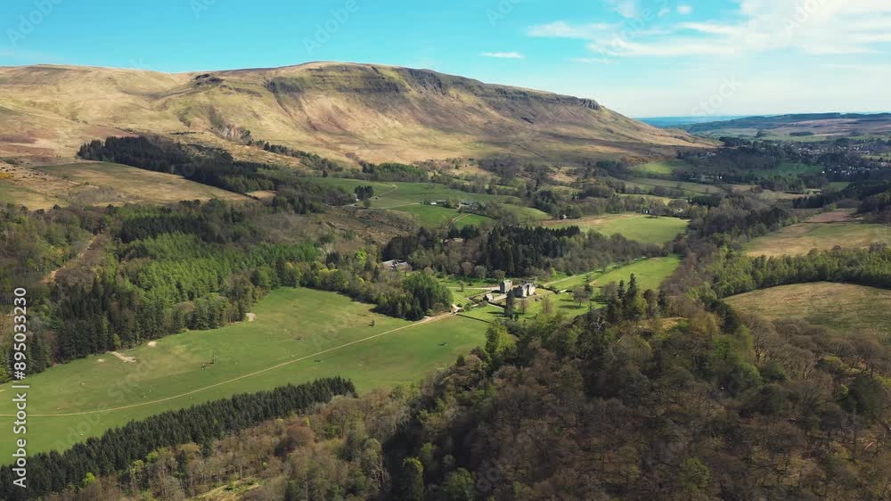 Aerial shot of beautiful valley in the British countryside, Lush green fields, British castle, pine tree forest and hills surrounding on a sunny spring day Aerial shot of beautiful valley in the British countryside, Lush green fields, British castle, pine tree forest and hills surrounding on a sunny spring day