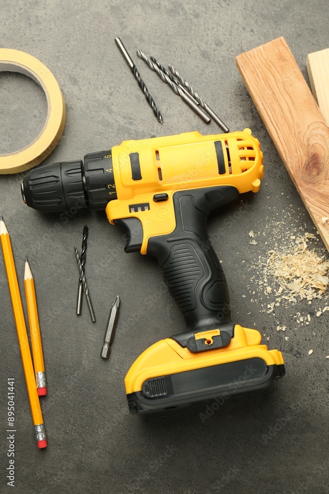Modern cordless electric drill, sawdust, planks and bits on grey table, flat lay Modern cordless electric drill, sawdust, planks and bits on grey table, flat lay