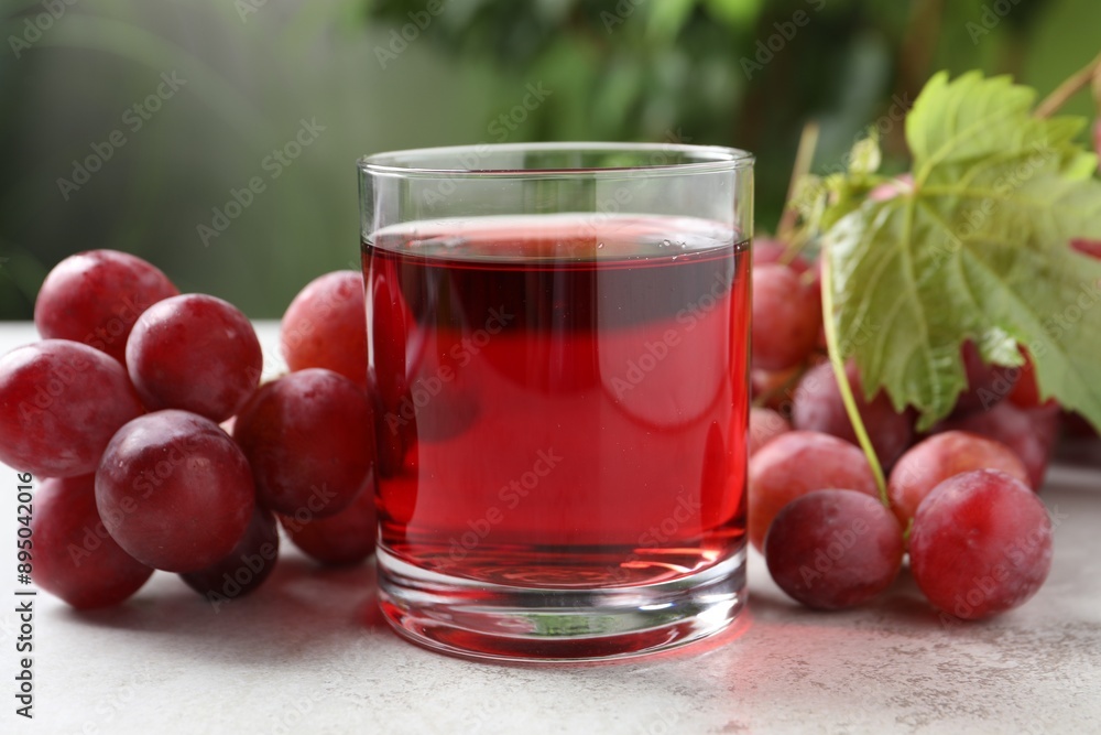 Tasty grape juice in glass, leaf and berries on light textured table against blurred green background, closeup Tasty grape juice in glass, leaf and berries on light textured table against blurred green background, closeup