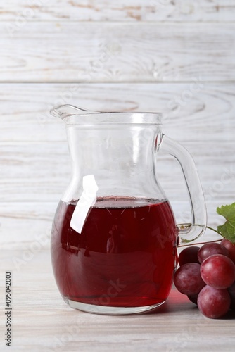 Tasty grape juice in jar and berries on light wooden table